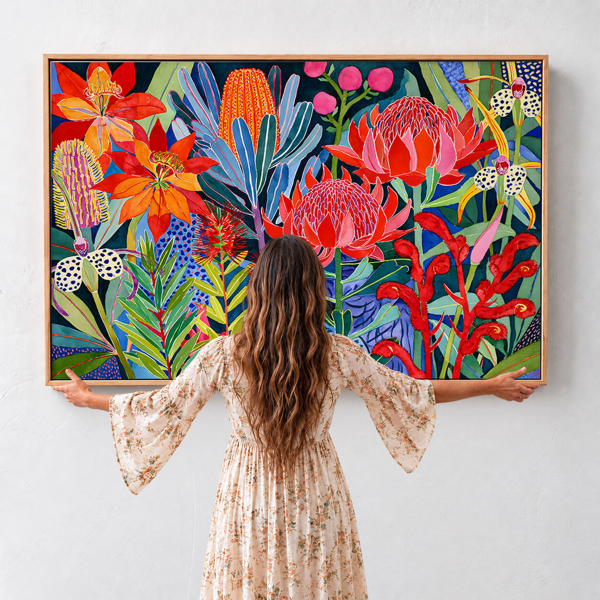 Large Australian native floral framed canvas with colourful proteas, banksias and wildflowers shown with woman for scale
