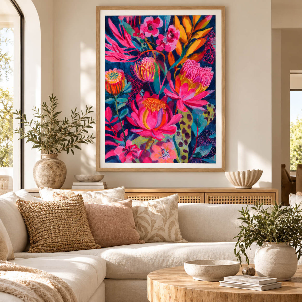 Large framed Australian botanical wall art with vibrant pink and orange flowers in a natural oak frame displayed in a modern living room.