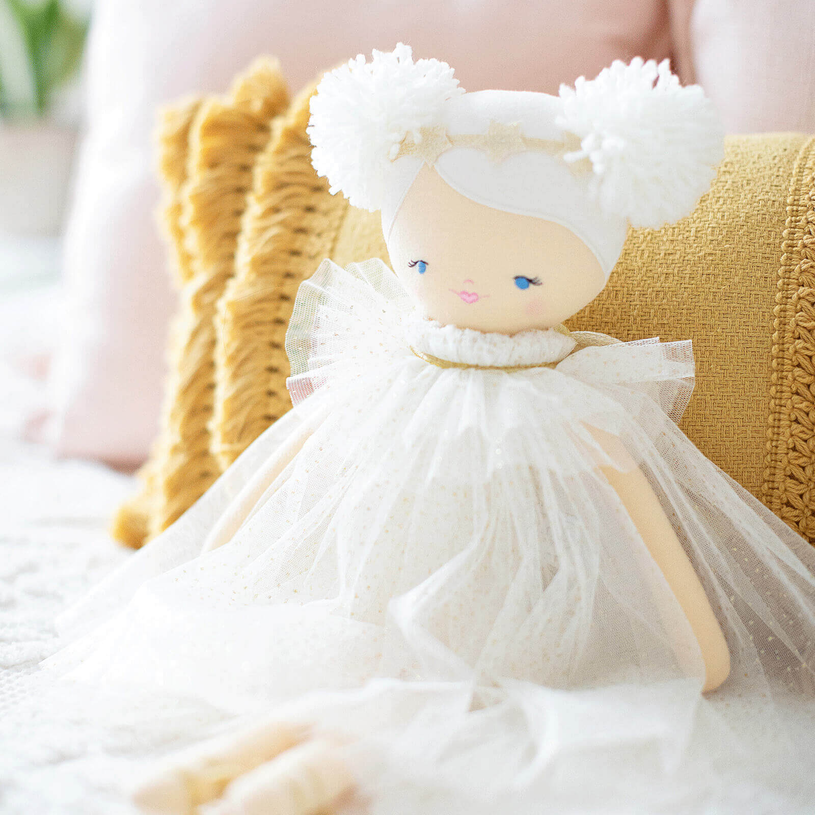 Doll wearing a white dress and white wool hair leaning against a yellow cushion