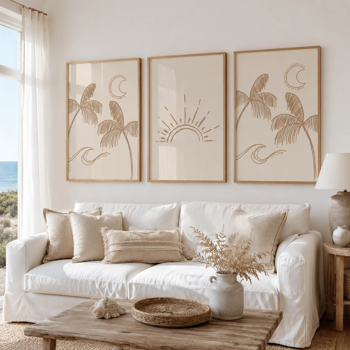 Modern coastal bedroom with a triptych of framed boho botanical and celestial prints above the bed, showcasing neutral palm tree, sunrise and ocean wave artwork in light oak frames.
